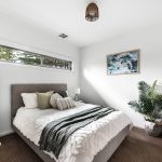 second bedroom with queen bed, neutral tones, plant in custom built home