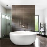 Large oval deep bath with tiled backdrop panel and modern fittings in a custom designed and built home