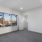 Grey Carpet beddroom with white walls and door opposite next to 3 sliding windows and downlights on ceiling