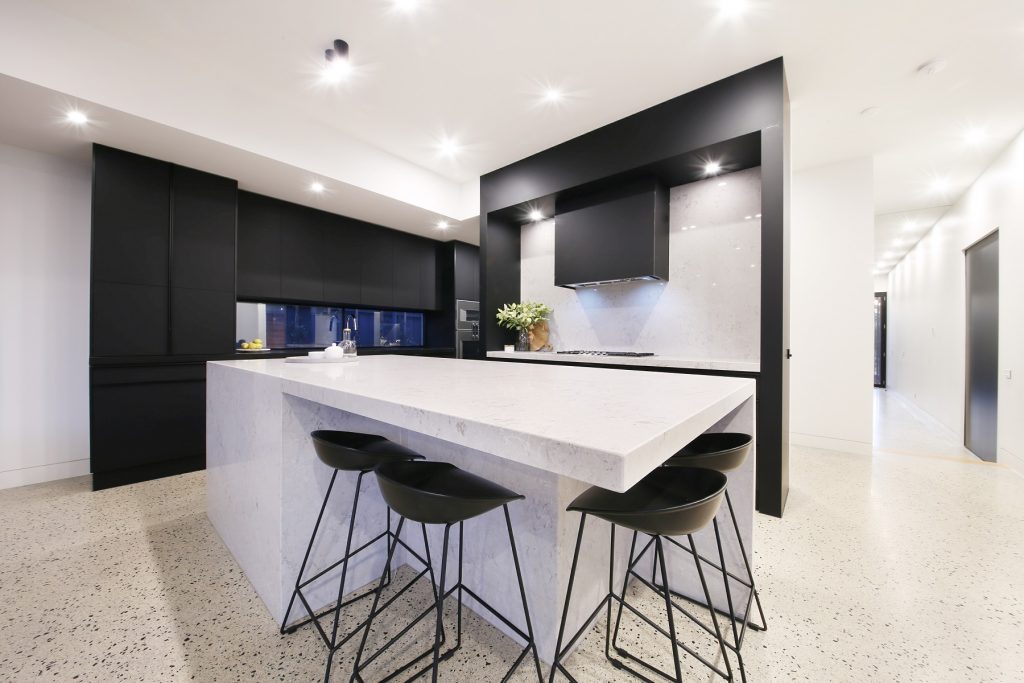 custom built home showing kitchen with cut polished concrete stone look floors, modern range hood, black accents and marble bench.