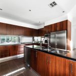 Wood panel kitchen with black granite bench tops, modern appliances and polished floors in custom built home