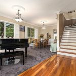 Open area with grand piano on left on grey carpet and floorboards adjoining with beautiflu stair case